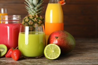 Photo of Glassware with different juices and fresh fruits on wooden background. Space for text