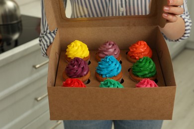 Woman holding box with delicious colorful cupcakes indoors, closeup