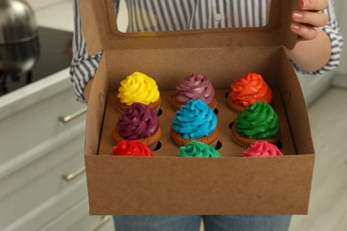 Photo of Woman holding box with delicious colorful cupcakes indoors, closeup