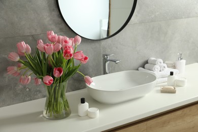 Photo of Vase with beautiful pink tulips and toiletries near sink in bathroom