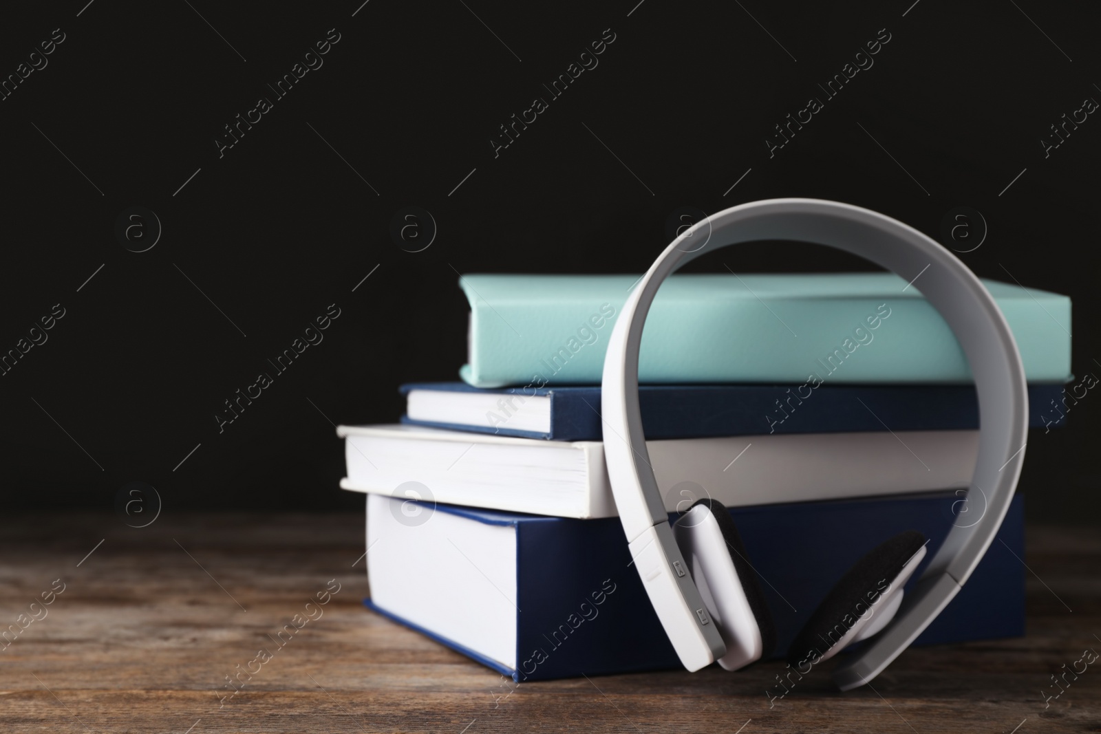 Photo of Modern headphones with hardcover books on wooden table. Space for text