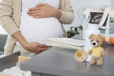 Photo of Pregnant woman near chest of drawers with packed bag for maternity hospital indoors, closeup
