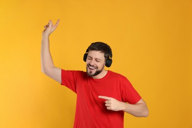 Photo of Happy man in headphones enjoying music and dancing on orange background
