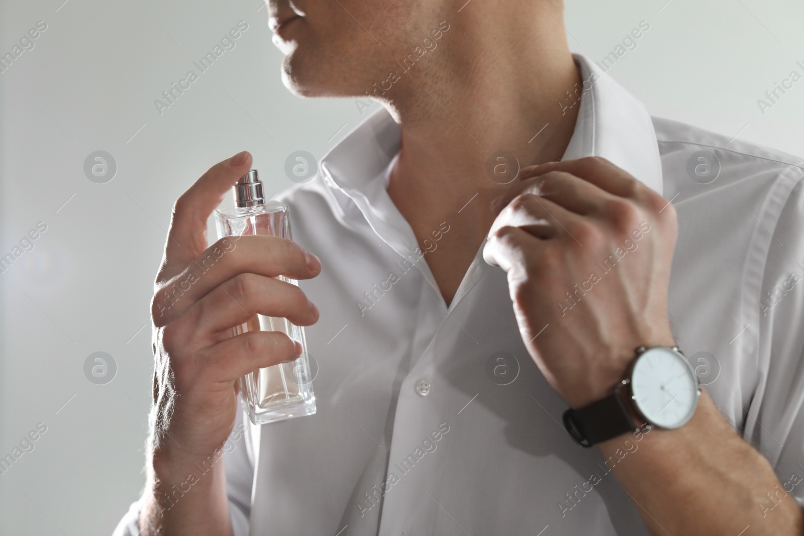 Photo of Handsome man applying perfume on neck against light background, closeup