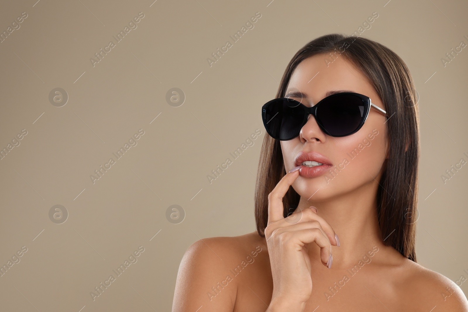 Photo of Beautiful young woman wearing sunglasses on beige background. Space for text