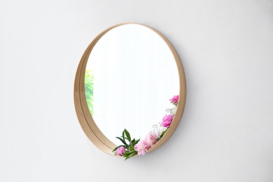 Round mirror with fresh flowers on white wall in modern room interior