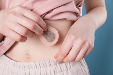 Photo of Woman applying contraceptive patch onto her body on blue background, closeup