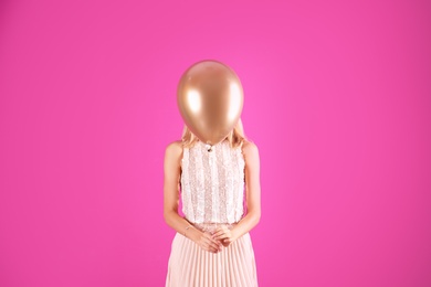 Young woman hiding behind air balloon on color background