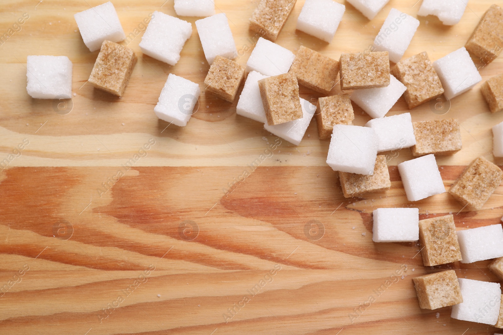 Photo of White and brown sugar cubes on wooden table, flat lay. Space for text