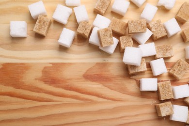 Photo of White and brown sugar cubes on wooden table, flat lay. Space for text