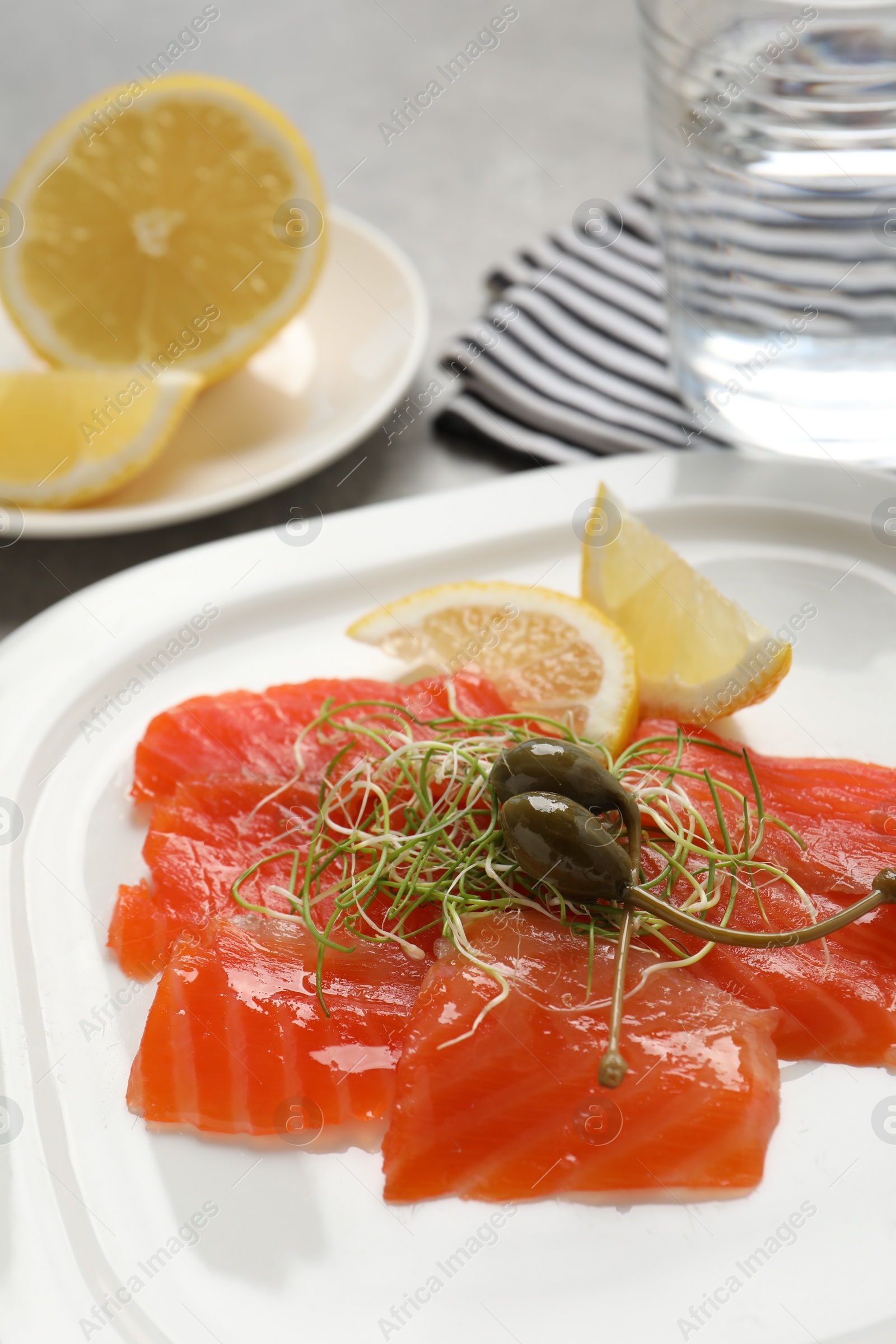 Photo of Salmon carpaccio with capers, microgreens and lemon on plate, closeup