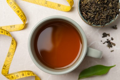 Flat lay composition with herbal diet tea and measuring tape on light marble table. Weight loss concept