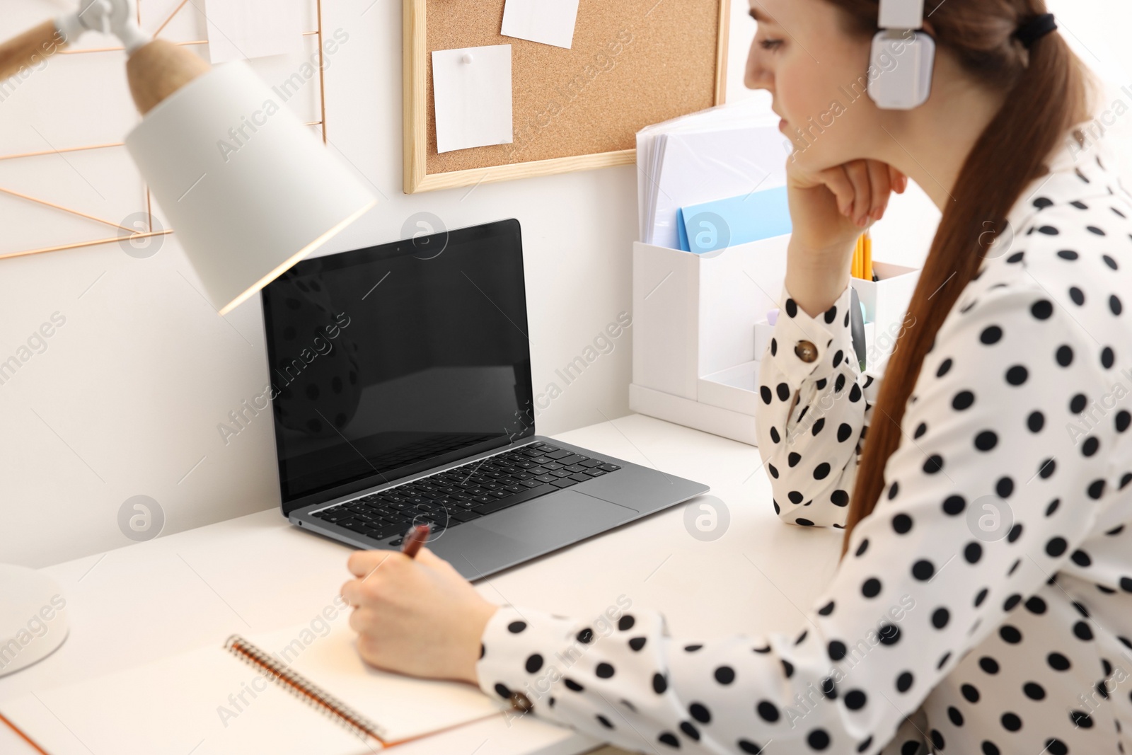 Photo of E-learning. Woman taking notes during online lesson at table indoors, closeup