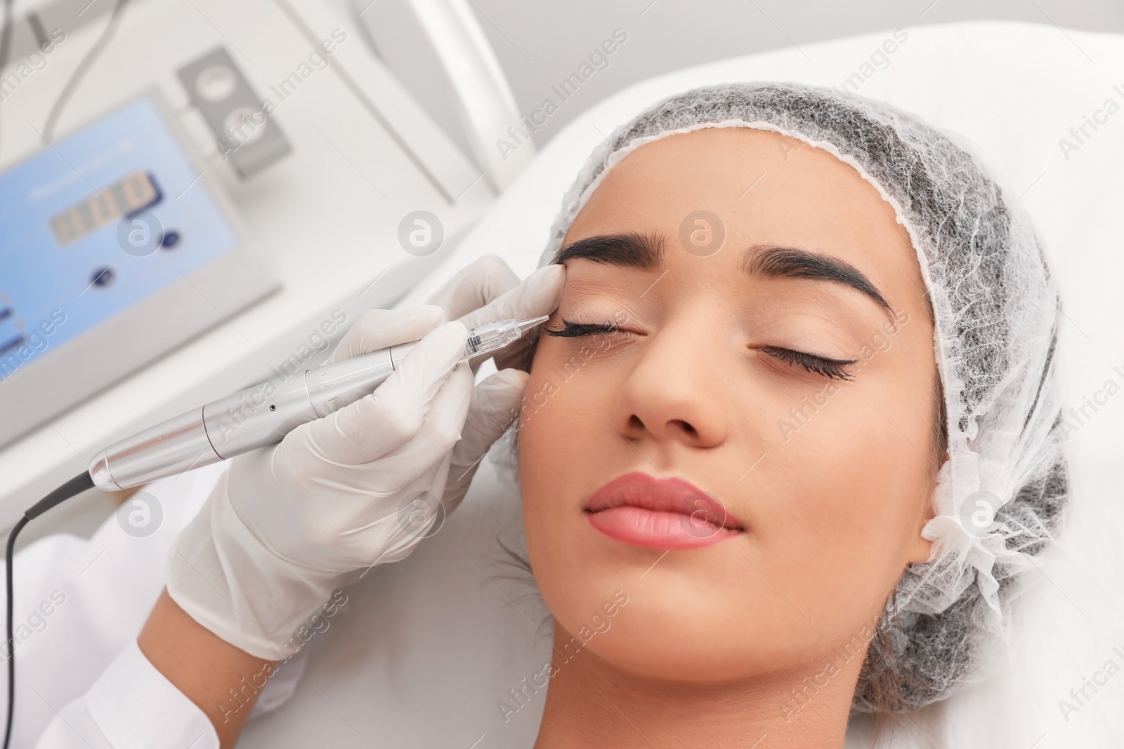 Photo of Young woman undergoing procedure of permanent eye makeup in tattoo salon