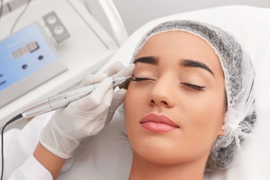 Young woman undergoing procedure of permanent eye makeup in tattoo salon