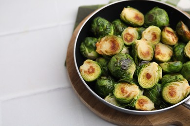 Photo of Delicious roasted Brussels sprouts in frying pan on white table, closeup. Space for text