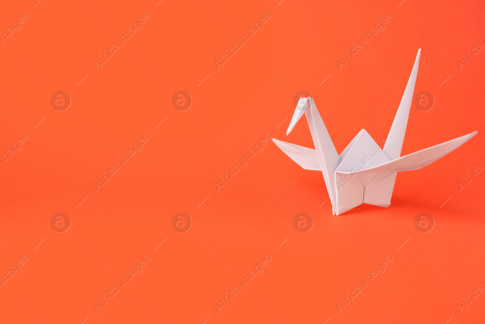 Photo of Origami art. Handmade paper crane on orange background, space for text