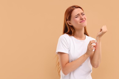 Photo of Suffering from allergy. Young woman scratching her arm on beige background, space for text