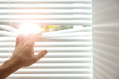 Photo of Young man opening window blinds, closeup. Space for text