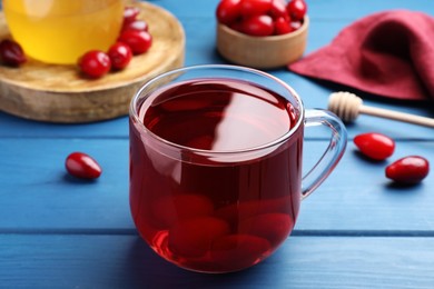 Photo of Glass cup of fresh dogwood tea with berries on blue wooden table