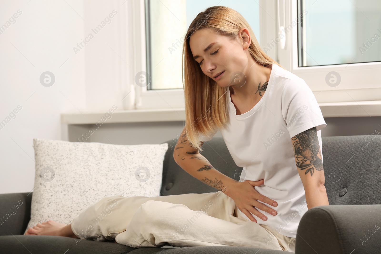 Photo of Young woman suffering from menstrual pain on sofa indoors