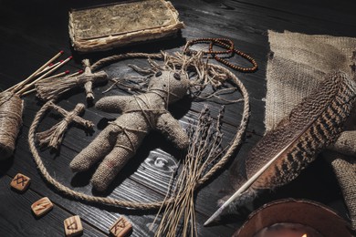 Photo of Female voodoo doll with pins surrounded by ceremonial items on black wooden background