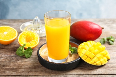 Photo of Glass of fresh mango drink and tropical fruits on wooden table