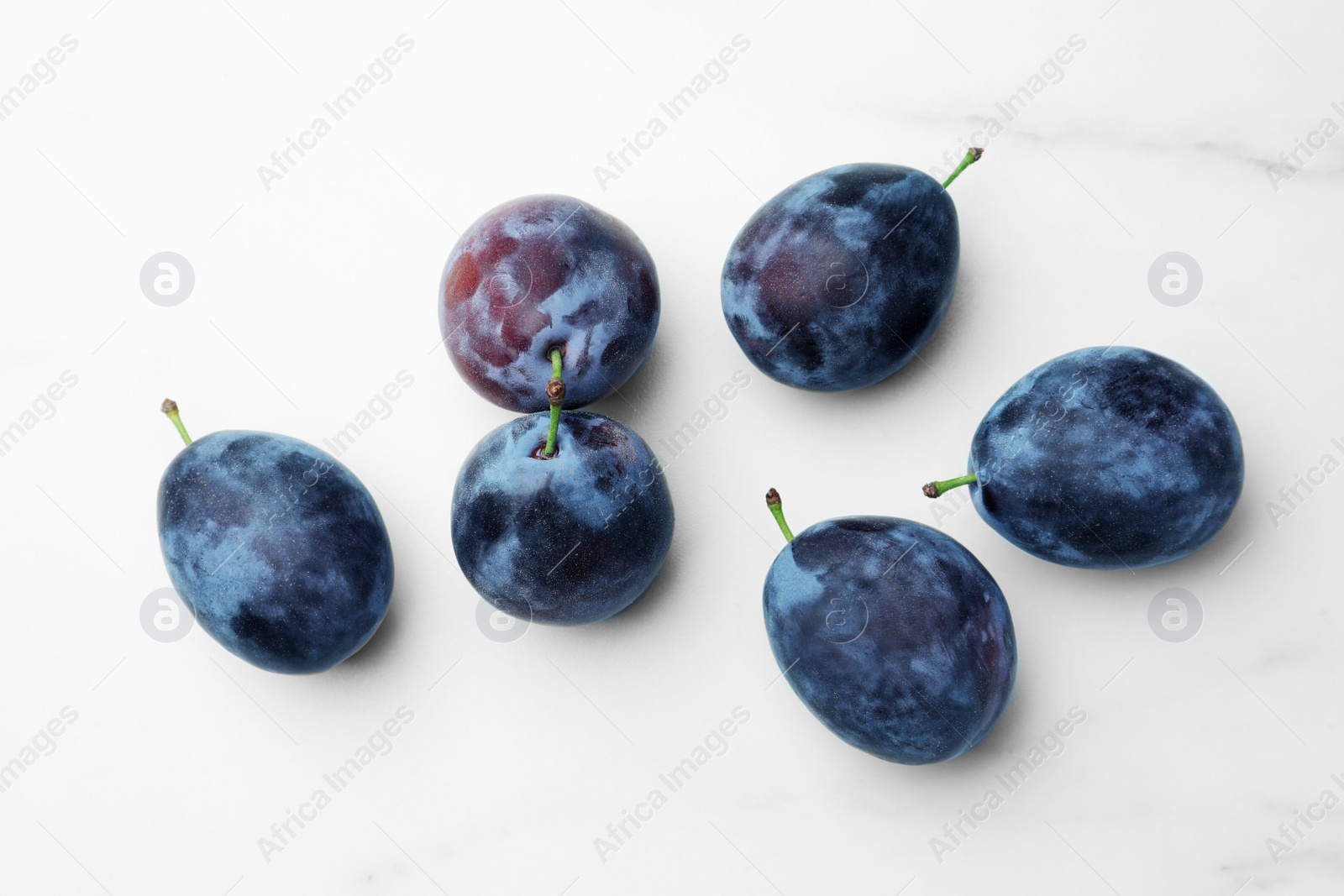 Photo of Tasty ripe plums on white marble table, flat lay