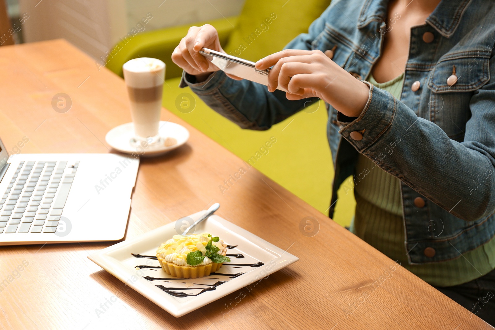 Photo of Blogger taking picture of cake at wooden table in cafe, closeup