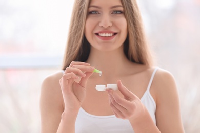 Woman holding contact lens with case on light background