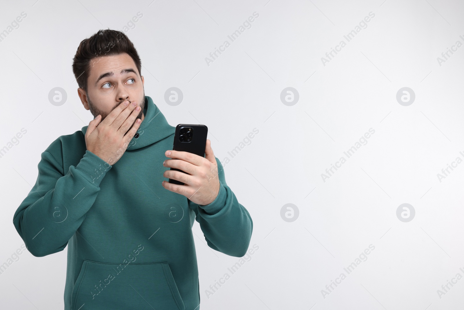 Photo of Shocked young man using smartphone on white background, space for text