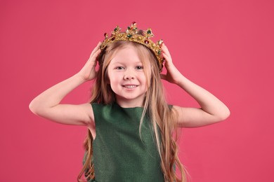 Photo of Cute girl in golden crown with gems on pink background. Little princess