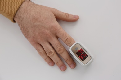 Man measuring oxygen level with modern fingertip pulse oximeter at white table, top view