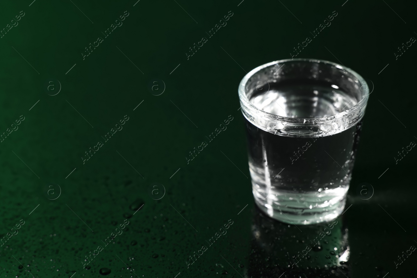 Photo of Glass of vodka on dark wet table, space for text