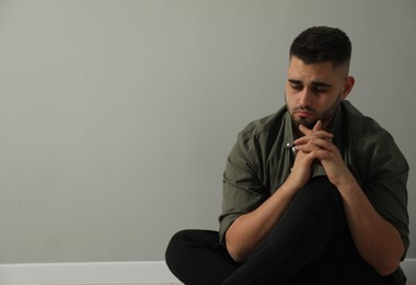 Sad man sitting near light grey wall. Space for text