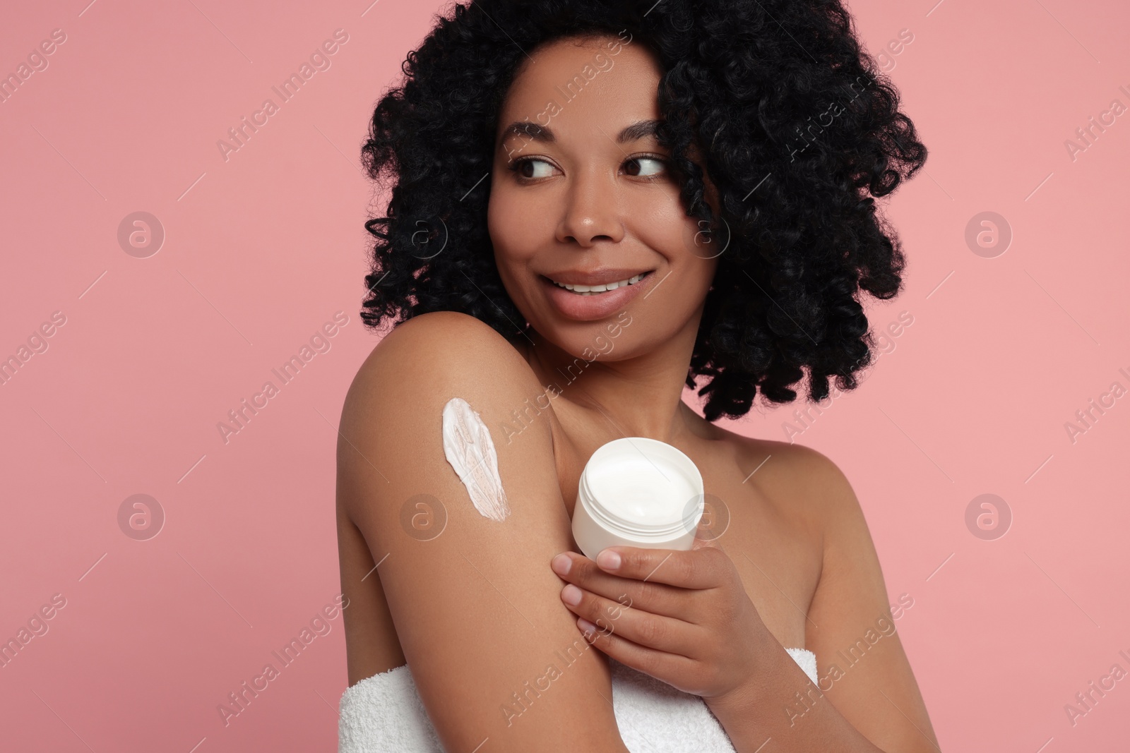 Photo of Young woman applying body cream onto arm on pink background