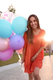 Cheerful young woman with color balloons outdoors on sunny day