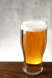 Glass with fresh beer on wooden table against light background