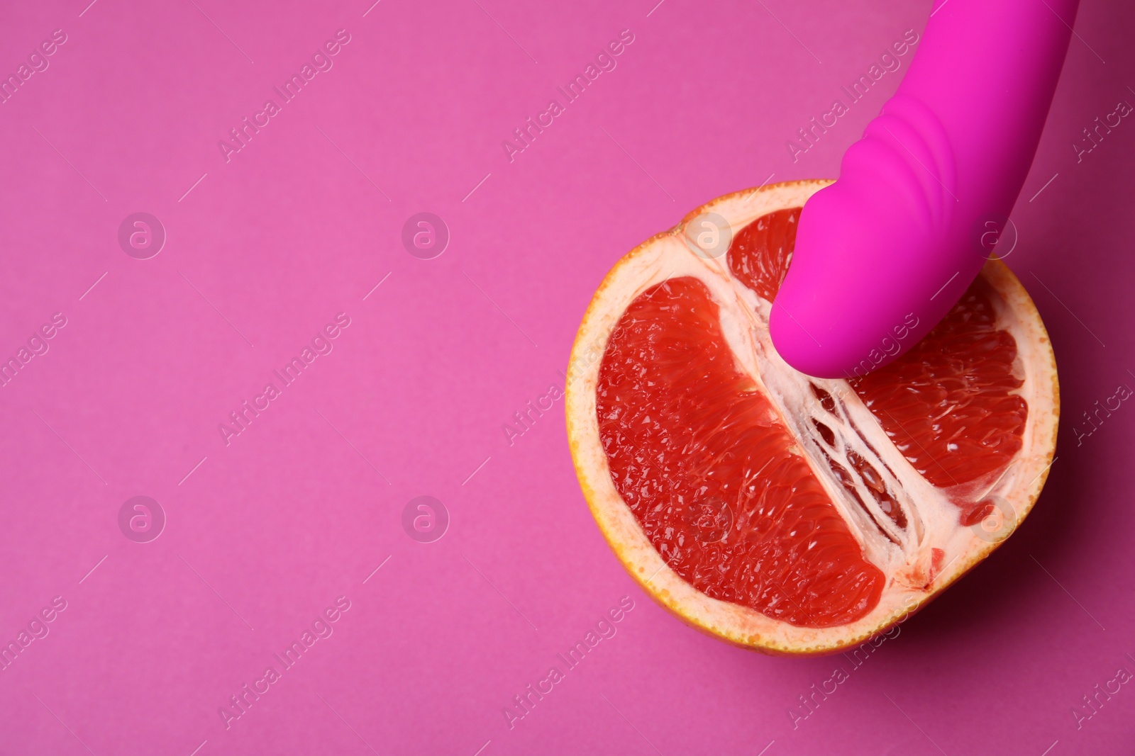 Photo of Half of grapefruit and vibrator on purple background, flat lay with space for text. Sex concept