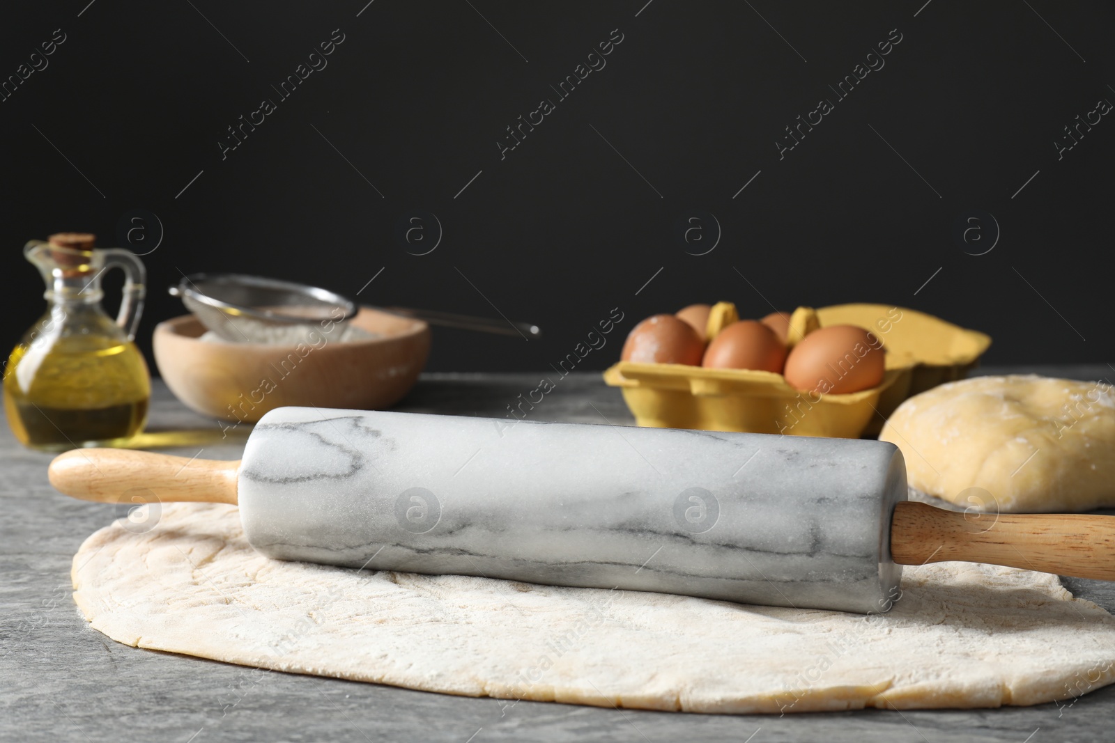 Photo of Raw dough, rolling pin and ingredients on grey table