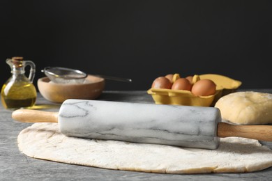 Raw dough, rolling pin and ingredients on grey table