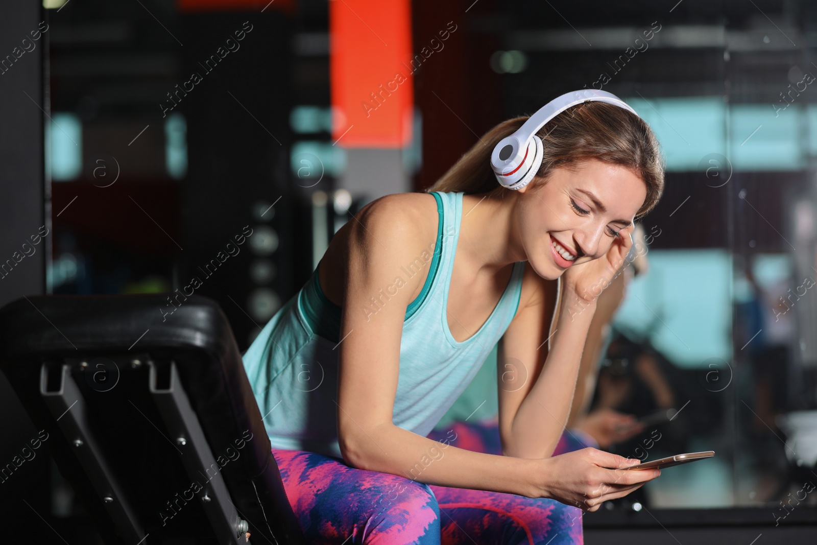Photo of Young woman with headphones listening to music on mobile device at gym