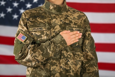 Photo of Female American soldier holding hand over heart with flag of USA on background, closeup. Military service