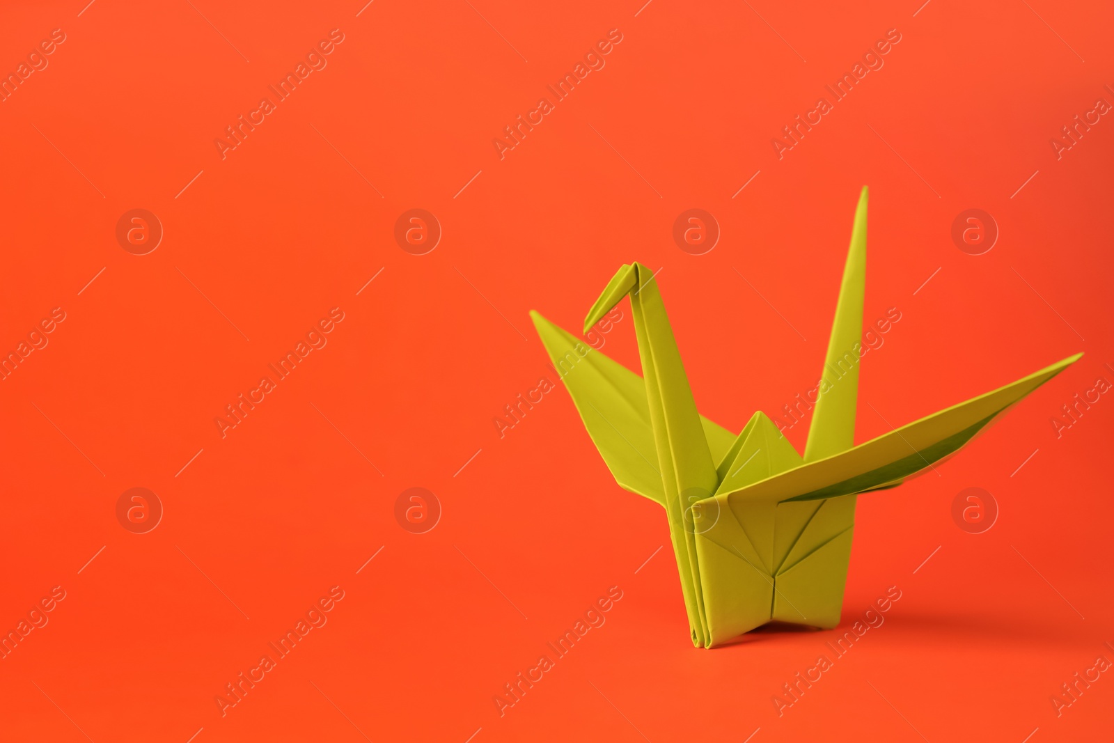 Photo of Origami art. Handmade paper crane on orange background, space for text
