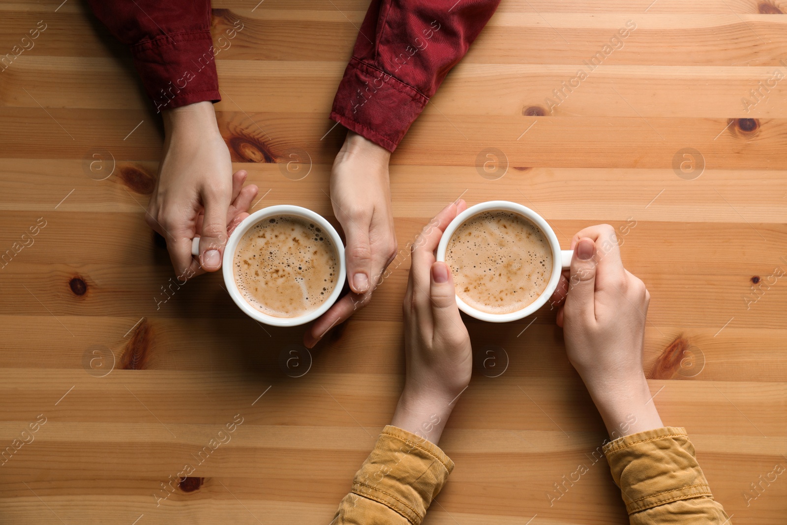 Photo of Women with cups of coffee at wooden table, top view