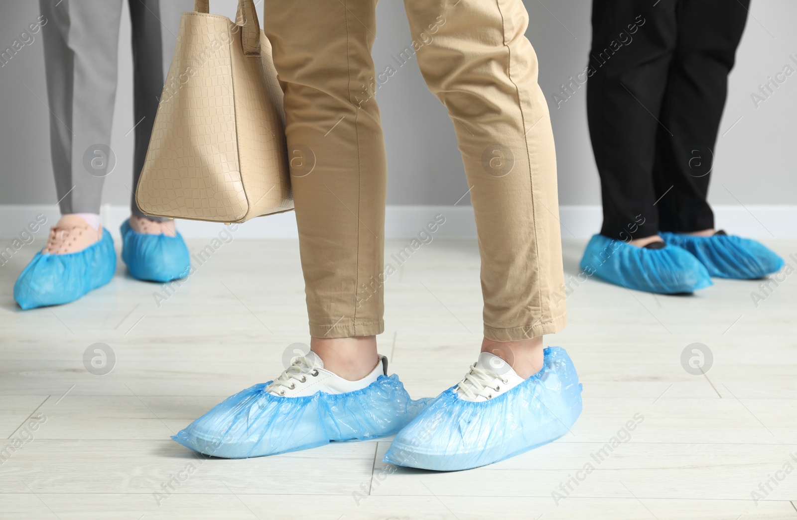 Photo of Women wearing blue shoe covers onto different footwear indoors, closeup