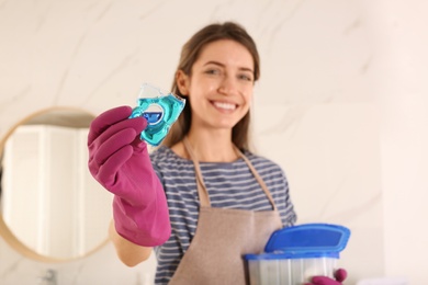 Happy woman holding laundry detergent capsule indoors, focus on hand