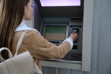 Photo of Young woman using cash machine for money withdrawal outdoors, focus on hand