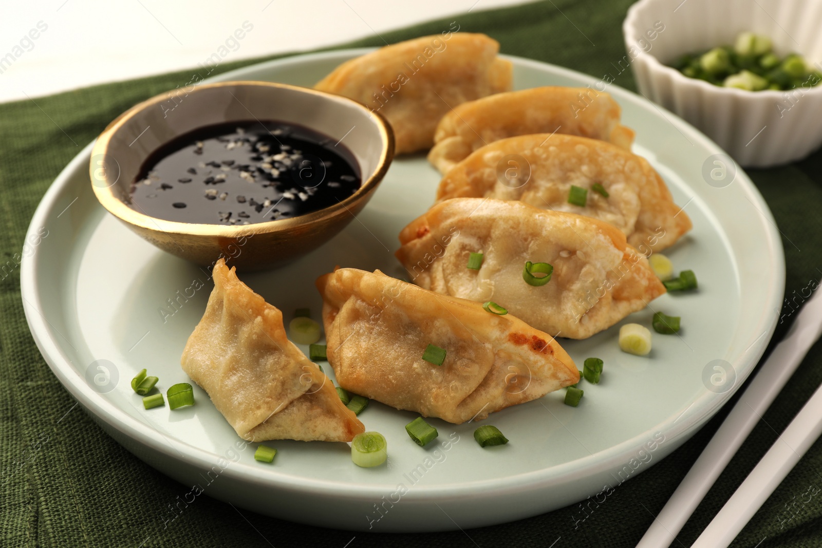 Photo of Delicious gyoza (asian dumplings) with green onions, soy sauce and chopsticks on table, closeup