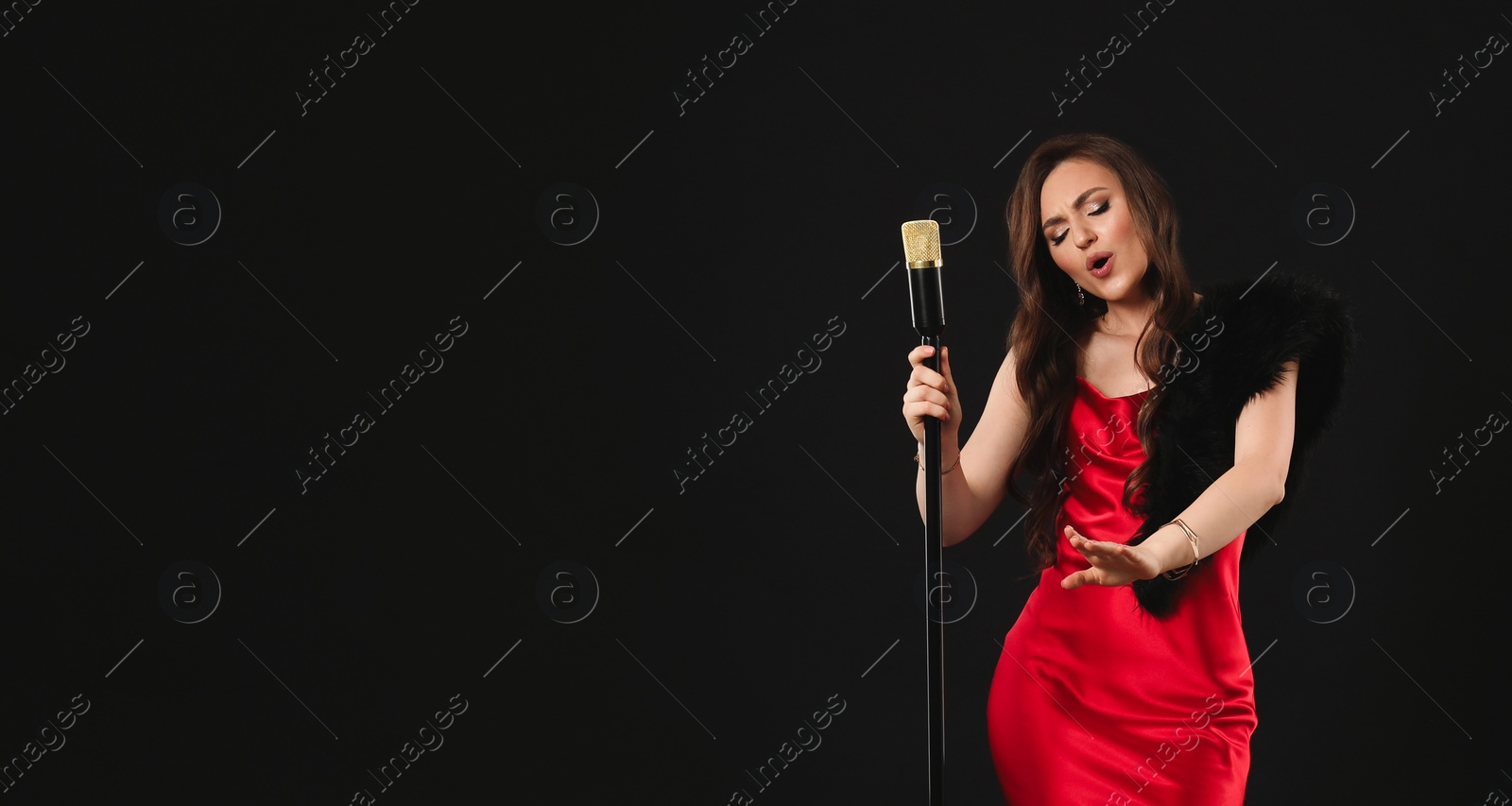 Photo of Beautiful young woman in stylish dress with microphone singing on black background